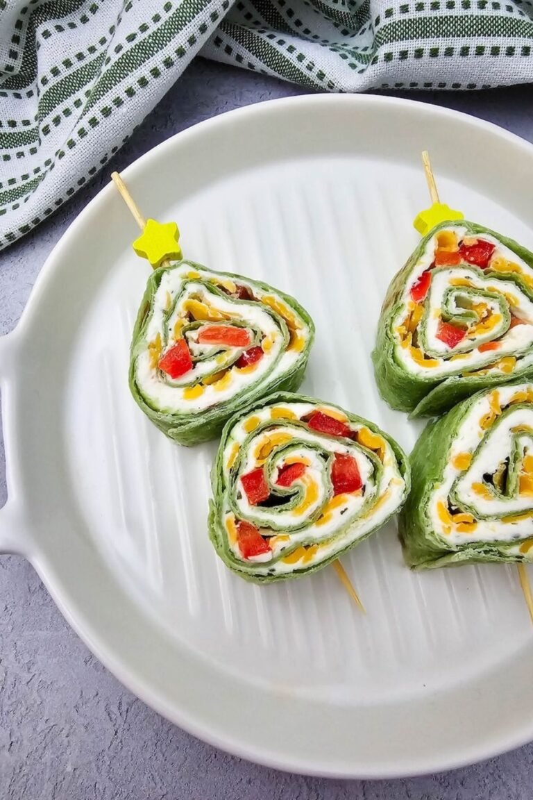Christmas tree pinwheels made with spinach tortillas, cream cheese, cheddar cheese, and red peppers served on skewers