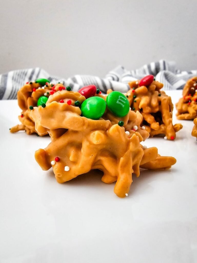 Close-up of a no-bake Christmas haystack cookie made with butterscotch, chow mein noodles, and topped with red and green M&Ms and sprinkles.