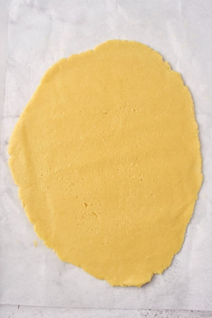 Rolled-out sugar cookie dough on parchment paper, ready to cut into shapes for Christmas cookies.