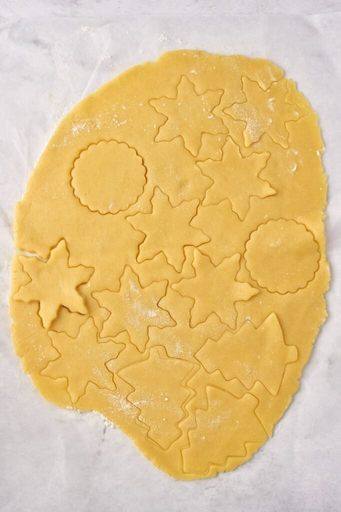 Christmas sugar cookie dough rolled out and cut into festive shapes like stars and trees using cookie cutters.