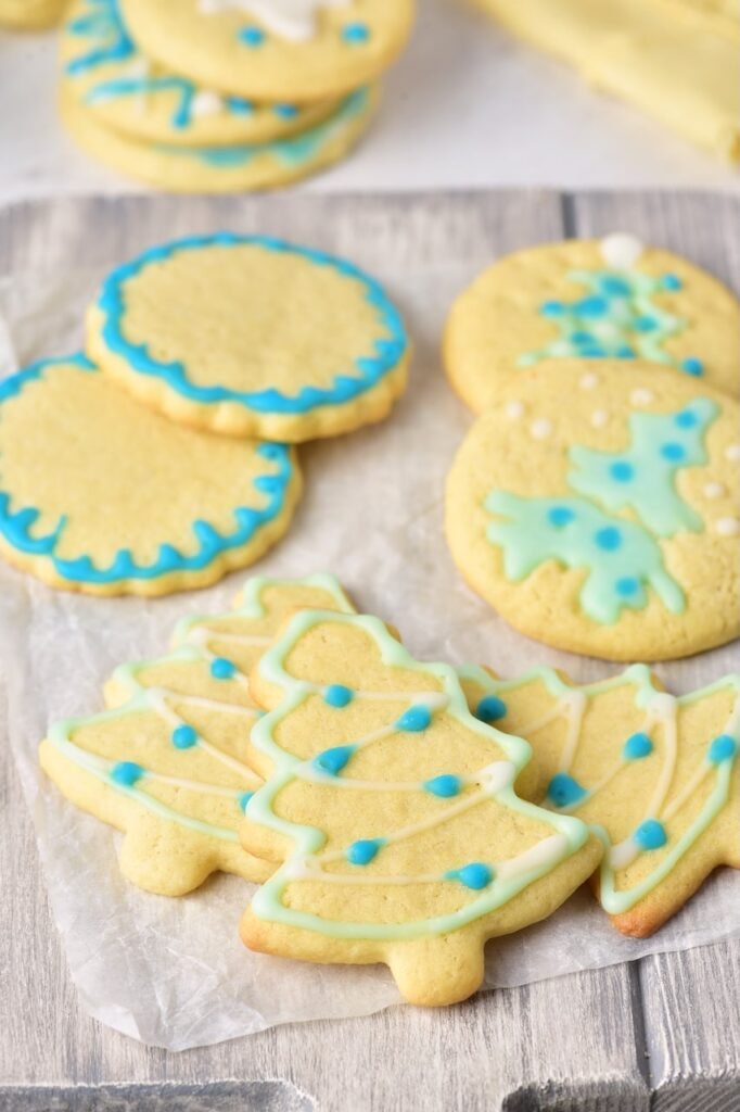 Decorated Christmas sugar cookies with blue and green icing in round and Christmas tree shapes on parchment paper.