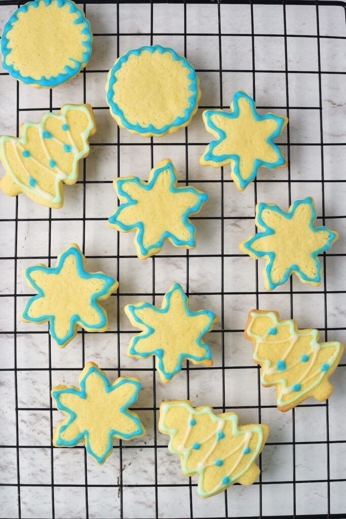Decorated Christmas sugar cookies with blue and white icing in tree and snowflake shapes cooling on a wire rack.