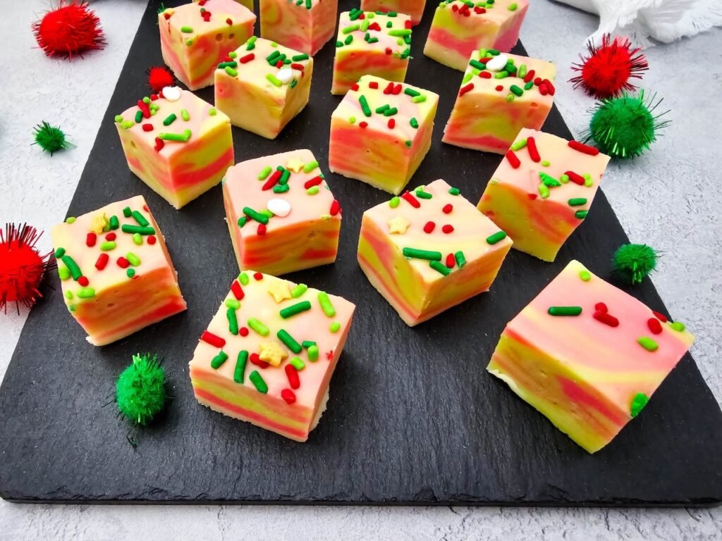 Pieces of easy swirled Christmas fudge with red and green sprinkles displayed on a black slate board for a festive holiday treat.