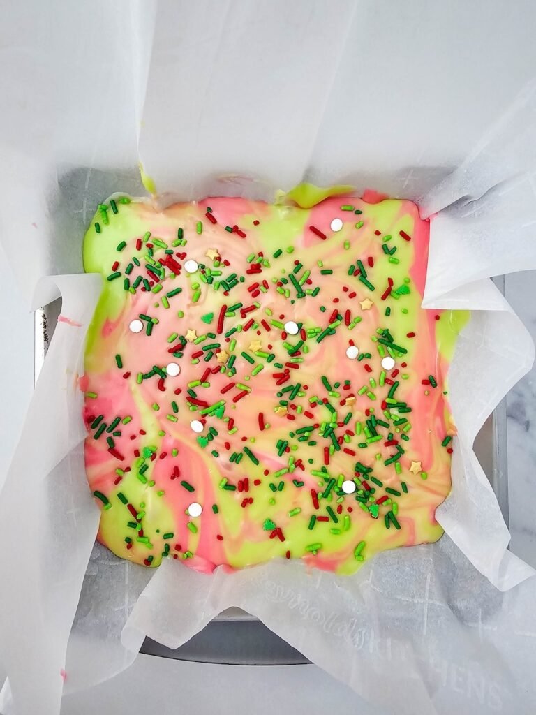 Festive red, green, and white treat topped with holiday sprinkles in a parchment-lined pan before chilling.