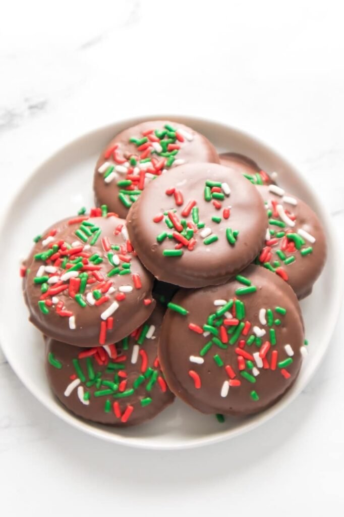 Overhead view of homemade Christmas Thin Mint Cookies topped with red, green, and white sprinkles on a white plate, showing a festive and easy no-bake holiday cookie made with Ritz crackers and Andes mint chocolate.
