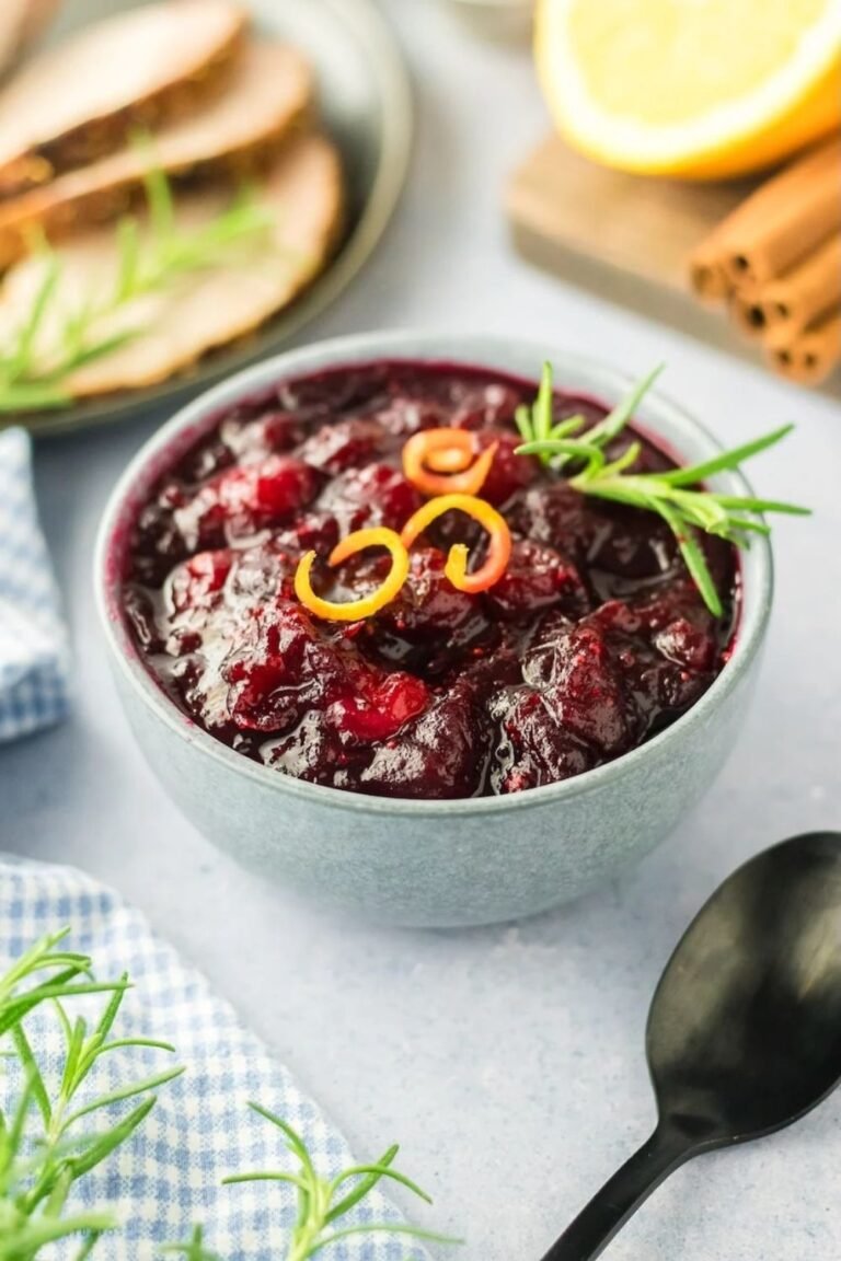 a bowl of homemade cranberry sauce garnished with orange zest and rosemary, ready to serve for Thanksgiving dinner.
