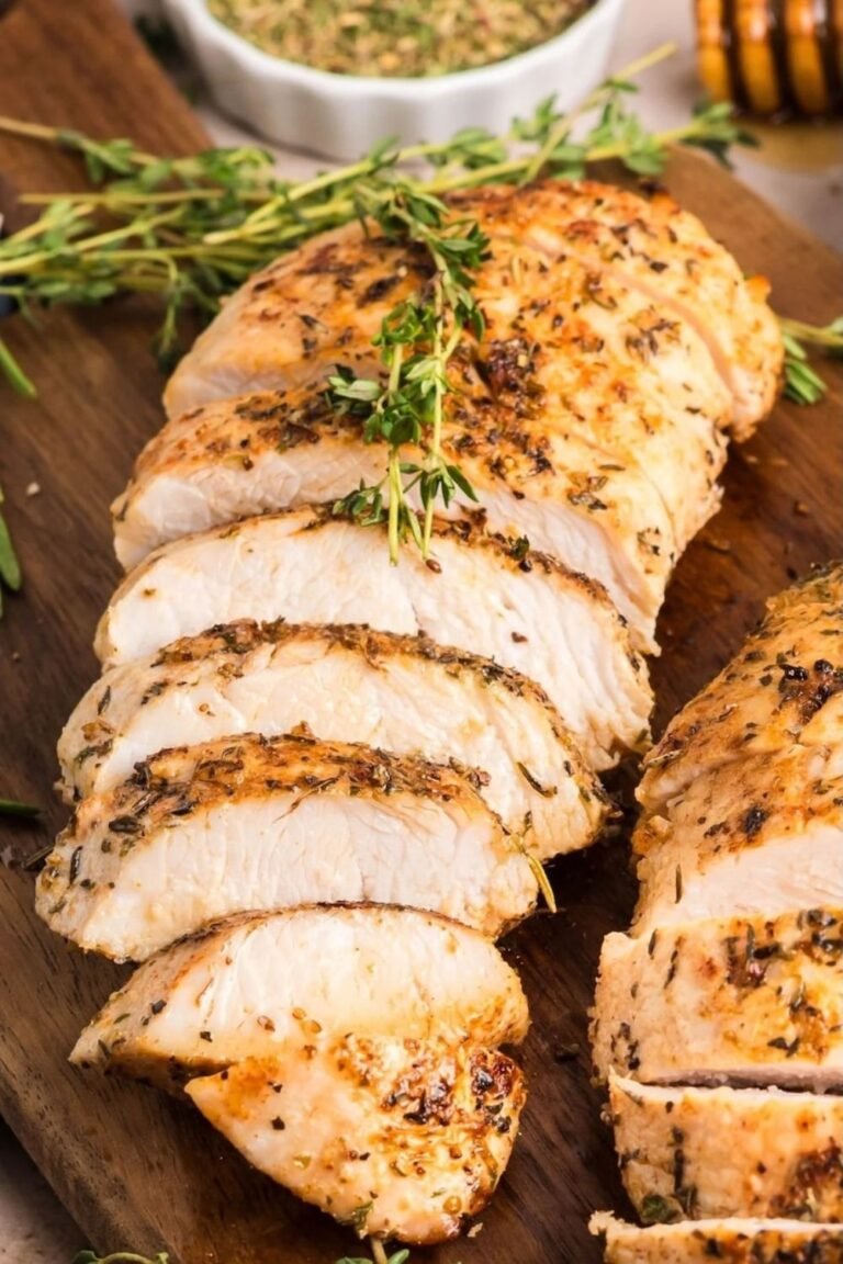 Sliced juicy oven roasted turkey breast tenderloin topped with fresh thyme on a wooden cutting board — an easy turkey breast recipe perfect for holidays or weeknight dinners.
