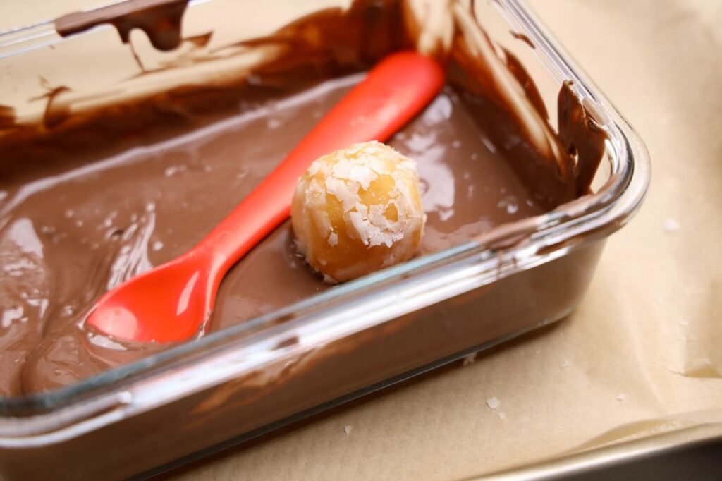 Fall treat sitting in melted chocolate with a red spoon during step one.