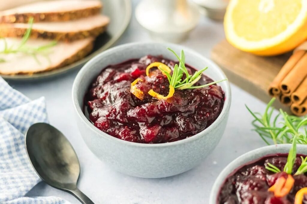 A bowl of easy homemade cranberry sauce with orange zest and rosemary, served beside slices of holiday turkey.