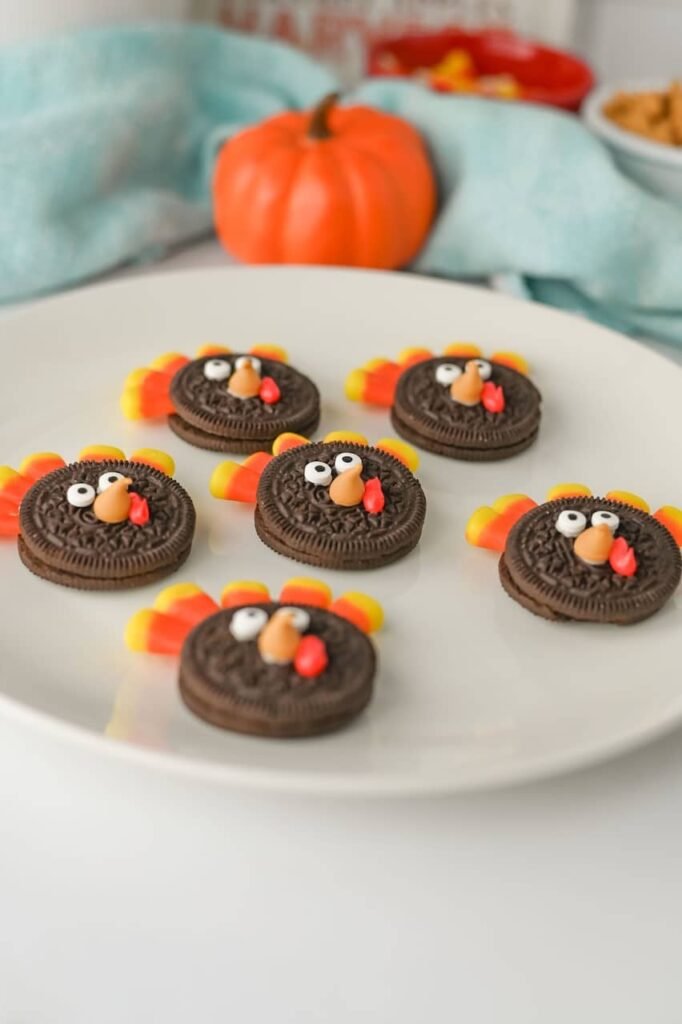 plate of finished Turkey Oreo Cookies decorated with candy corn feathers, candy eyes, and frosting beaks, with a small pumpkin and fall-themed background.