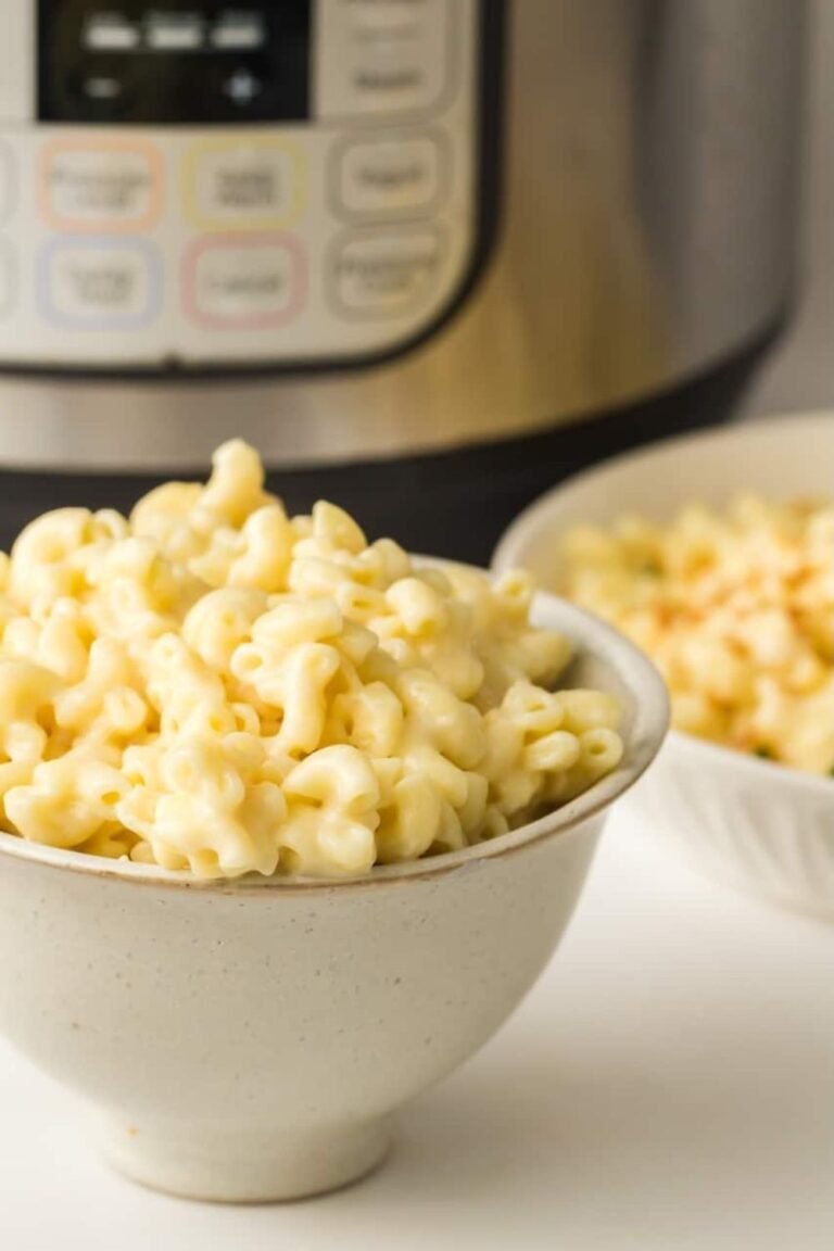 Bowl of creamy Instant Pot mac and cheese in front of the pressure cooker, ready to serve for an easy one-pot dinner.