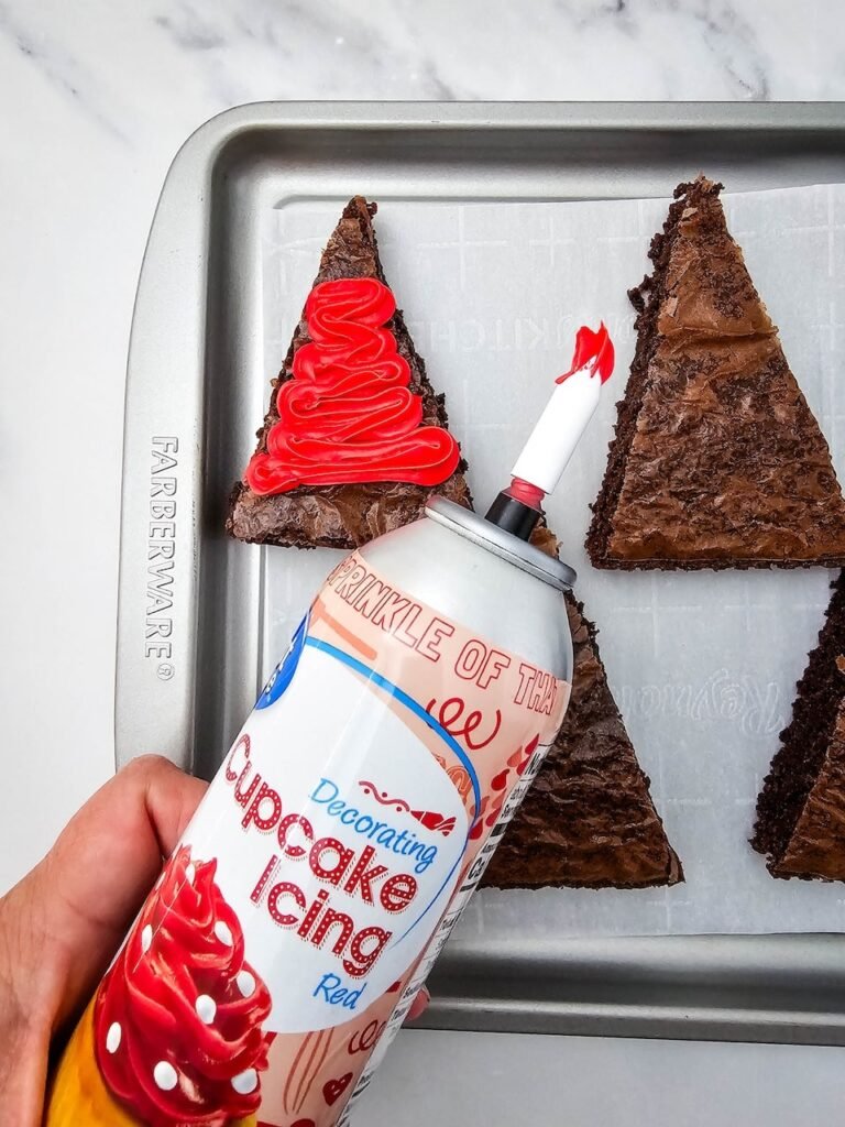 Piping red cupcake icing onto triangle brownies.