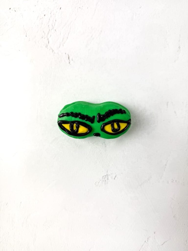 Fully decorated Grinch Nutter Butter cookie with yellow candy eyes and black chocolate eyebrows on a white background.