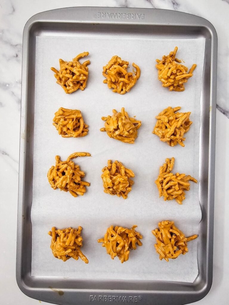 Scoops of haystack cookie mixture arranged on a parchment-lined baking sheet to set, ready for decorating as no-bake Christmas treats.