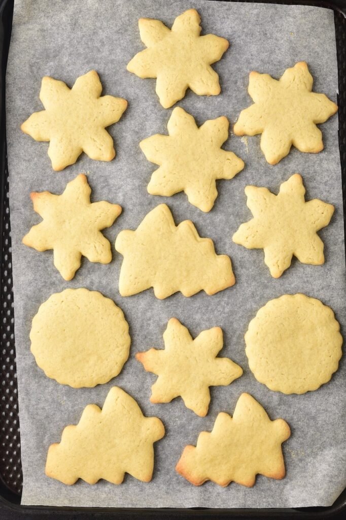 Freshly baked Christmas sugar cookies in tree and snowflake shapes cooling on a parchment-lined baking sheet.