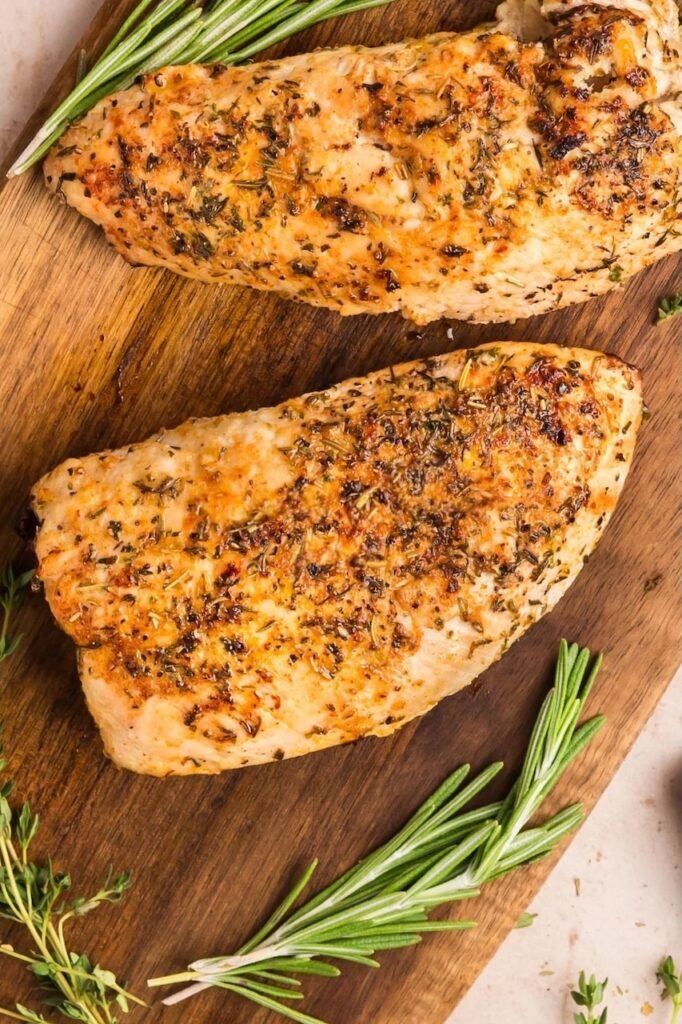 Close-up of golden herb roasted turkey tenderloins resting on a wooden cutting board with fresh rosemary and thyme — a juicy turkey breast recipe baked in the oven.