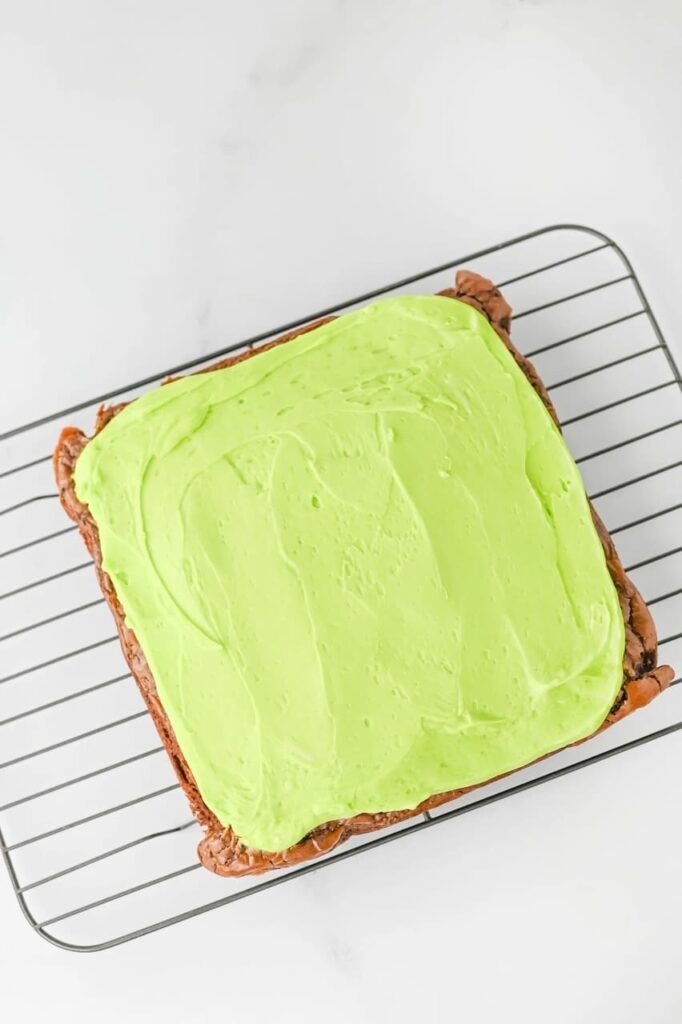 Freshly baked treats topped with bright green buttercream frosting cooling on a wire rack before adding sprinkles and decorations.