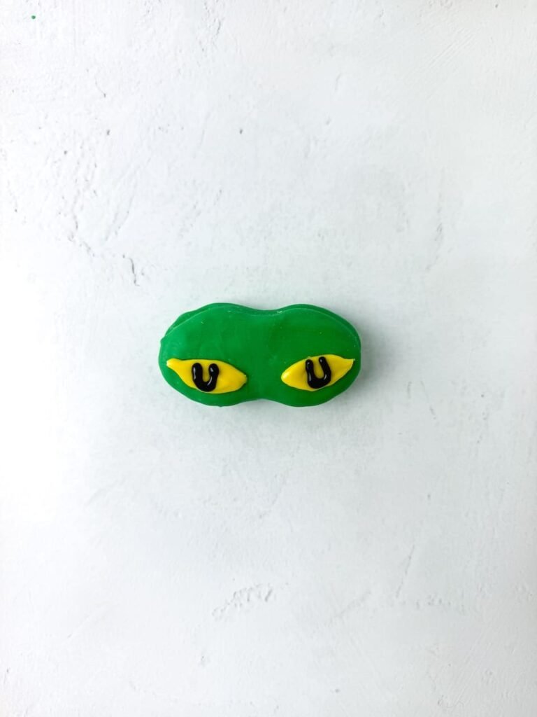 Green candy-coated cookie decorated with yellow and black eyes to resemble the Grinch.