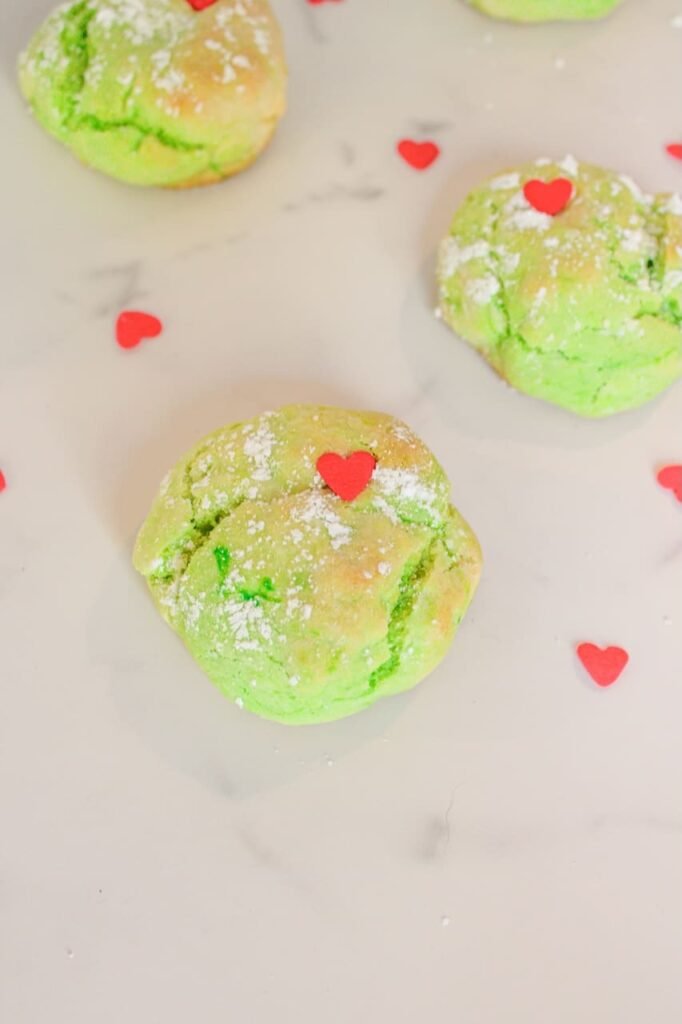 Close-up of a soft green Grinch Cookie topped with a red heart sprinkle and dusted with powdered sugar.