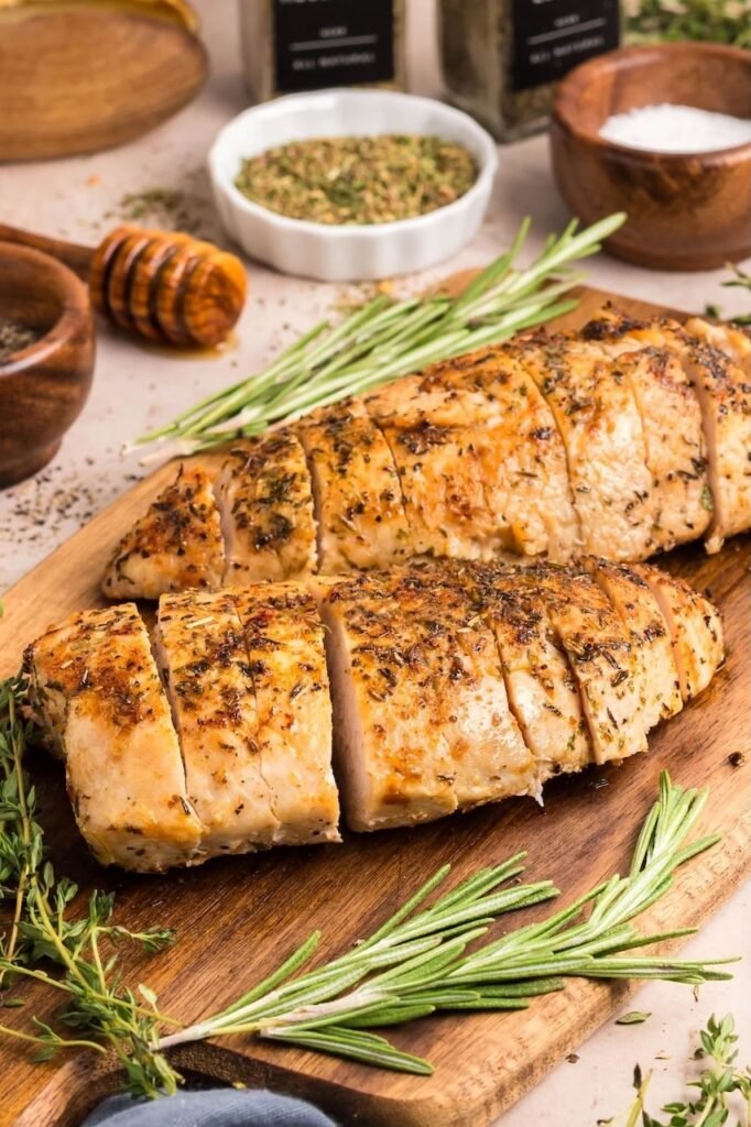 Juicy herb roasted turkey tenderloin sliced on a wooden board with rosemary, thyme, and honey in the background — an easy oven turkey recipe for weeknight dinners or holidays.