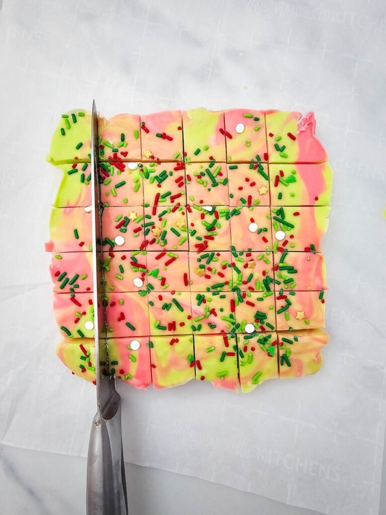 Cutting colorful red, green, and white swirled snack topped with sprinkles into small squares for gifting.