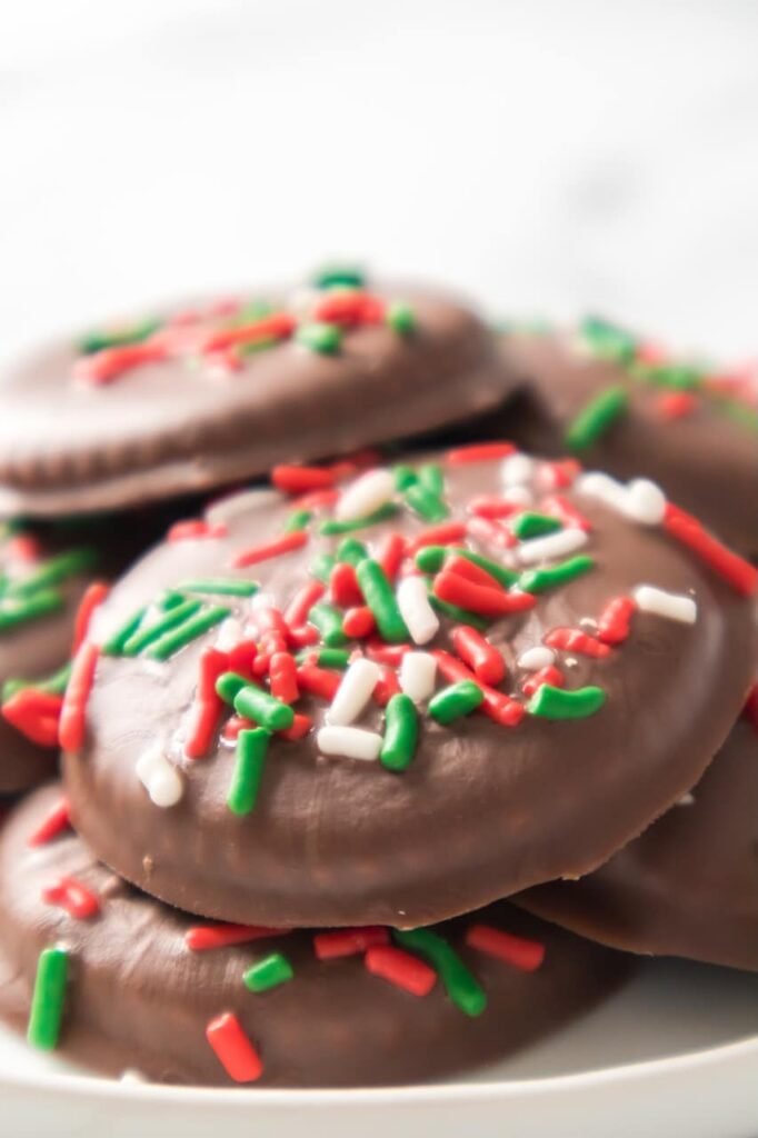 Close-up angled shot of stacked chocolate-covered Christmas Thin Mint Cookies decorated with red, green, and white sprinkles, showing the glossy finish and festive detail of this easy no-bake holiday cookie recipe.