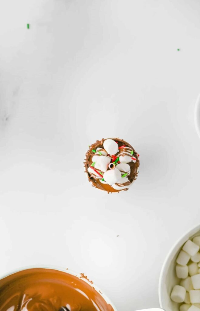 Step 6 of homemade hot chocolate sticks recipe — top of chocolate stick decorated with mini marshmallows and red and green Christmas sprinkles.