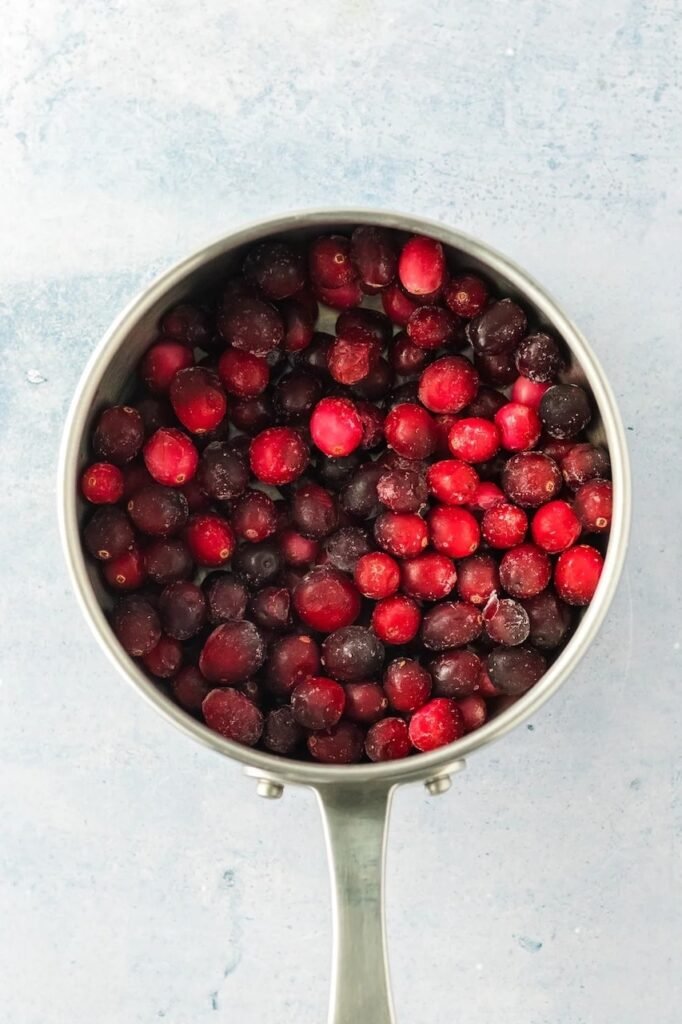 Step 2 — fresh cranberries added to a saucepan with sugar and water before simmering.