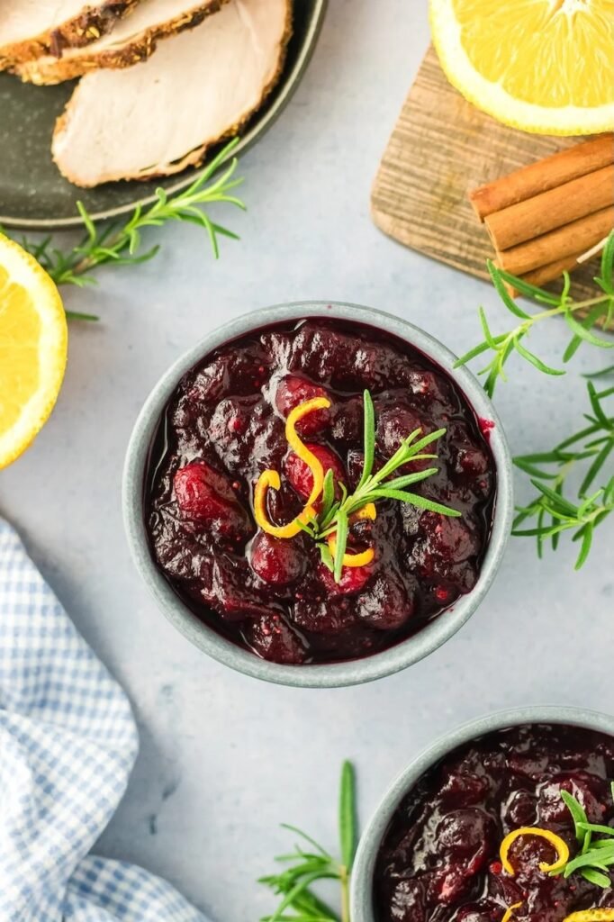 Step 4 of making homemade cranberry sauce — the finished sauce cooling in bowls, garnished with orange zest and rosemary.