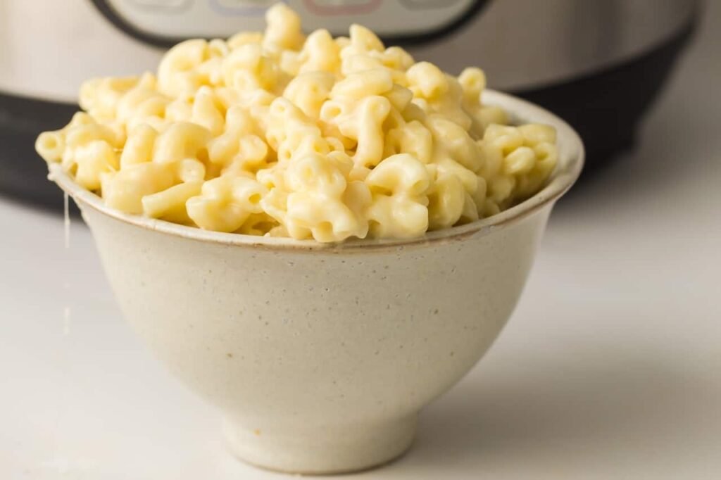 Close-up of creamy mac and cheese served in a white bowl with an Instant Pot in the background.
