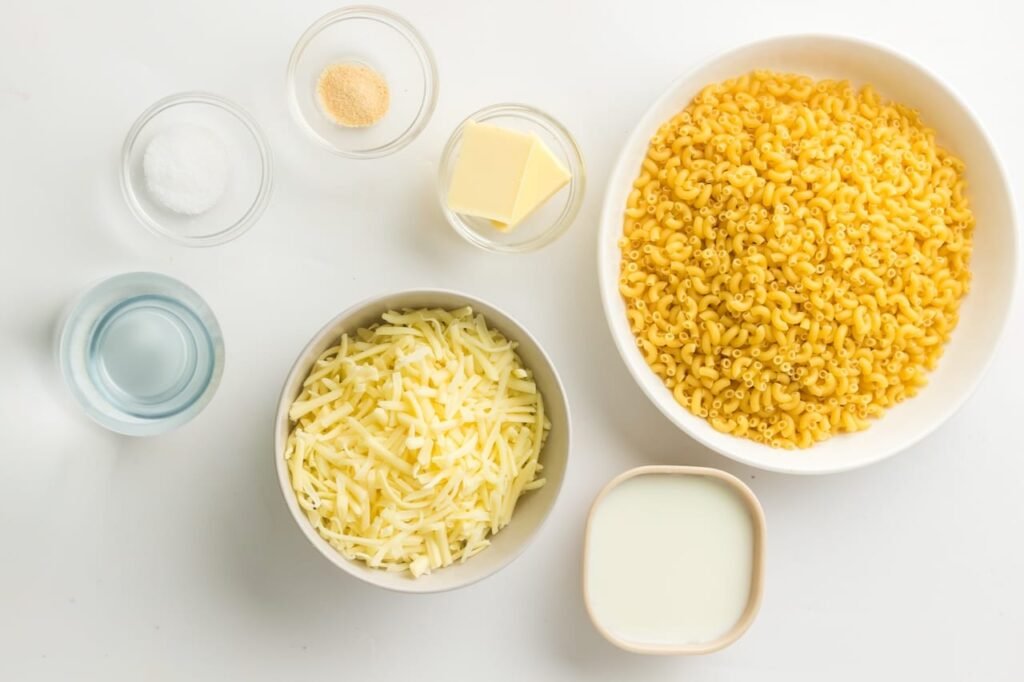 Ingredients for creamy Instant Pot mac and cheese, including pasta, cheese, milk, butter, and seasoning on a white counter.