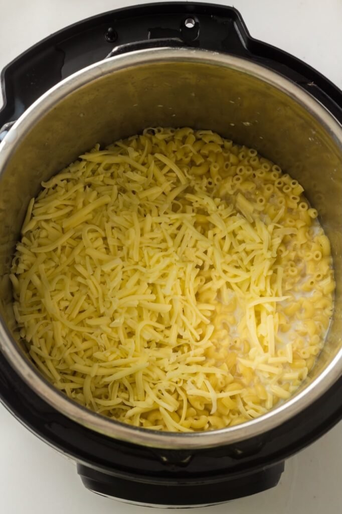 Cooked macaroni in an Instant Pot topped with freshly shredded cheese, ready to be stirred into a creamy mac and cheese sauce.