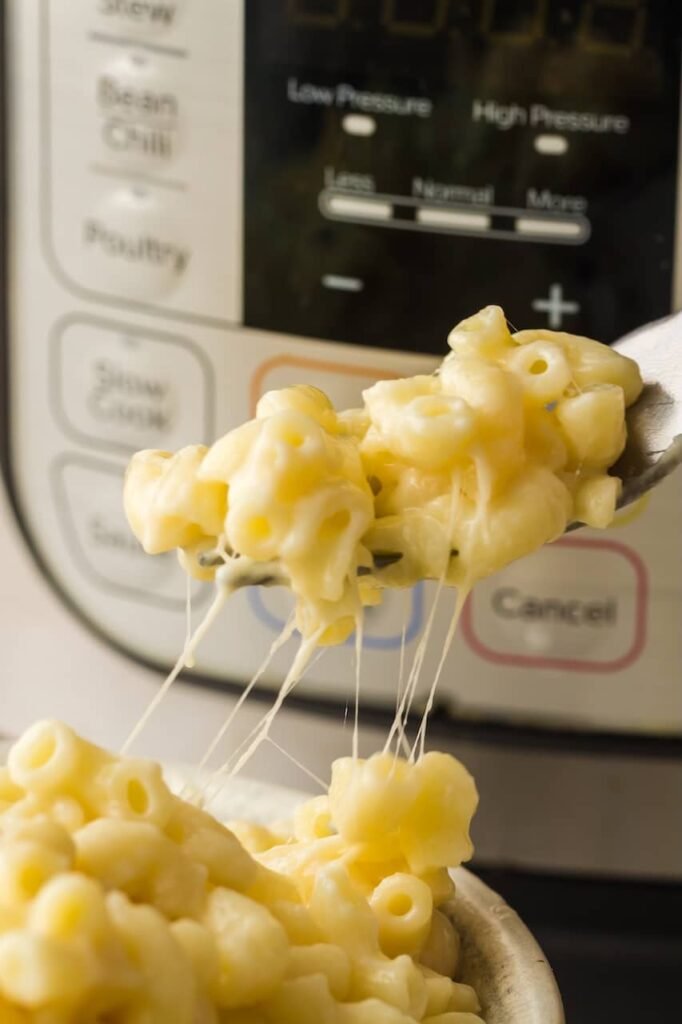 A spoon lifting creamy, cheesy macaroni from the Instant Pot, showing melted cheese stretching from the bowl.