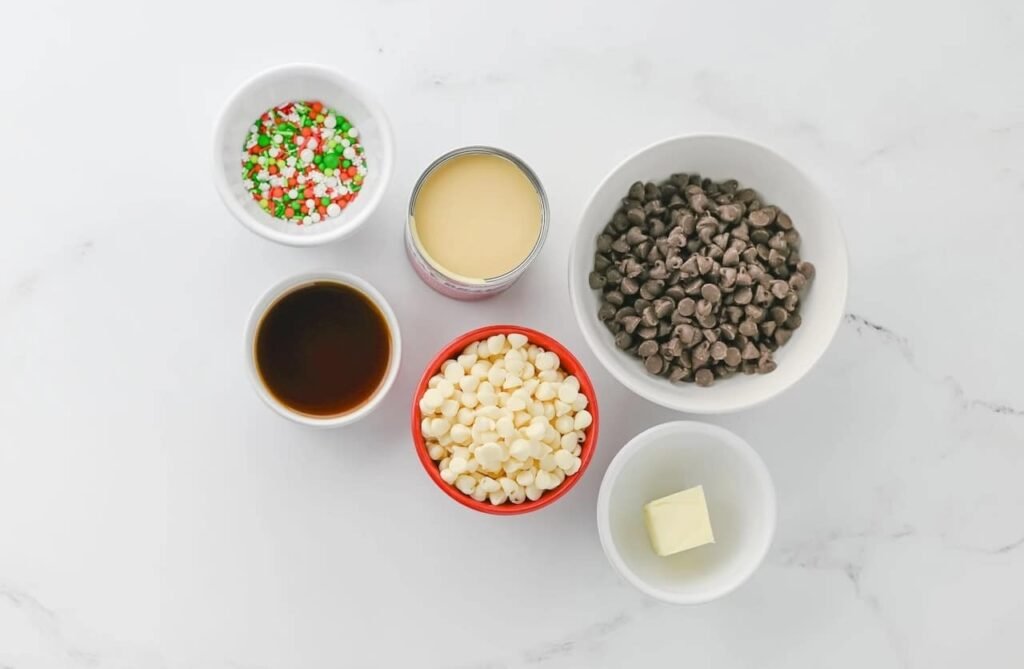 Ingredients for layered Christmas chocolate fudge including chocolate chips, white chocolate chips, sweetened condensed milk, butter, vanilla, and festive sprinkles.