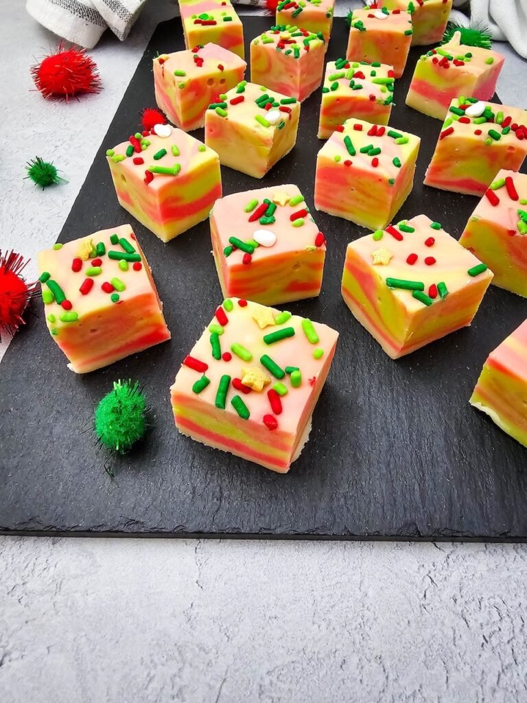 Close-up of creamy layered Christmas fudge squares with red and green sprinkles displayed on a slate board.