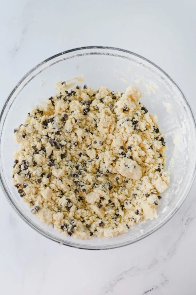 Chocolate chip snowball cookie dough in a glass bowl with mini chocolate chips evenly mixed throughout.