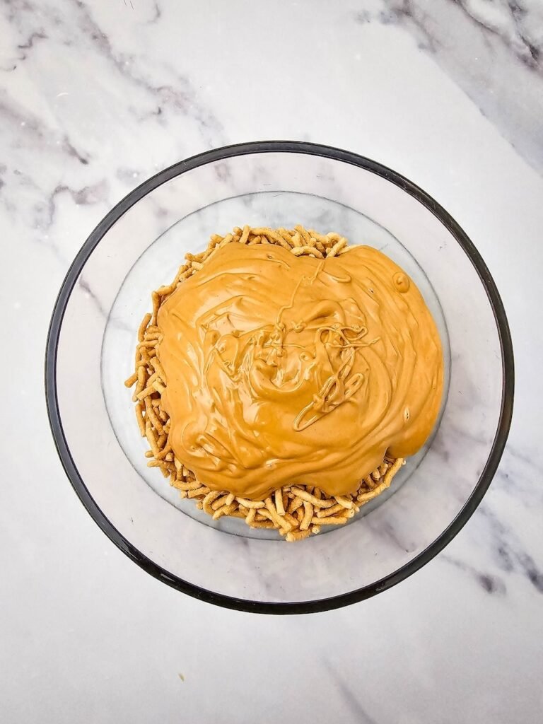 Melted butterscotch and peanut butter mixture poured over crunchy chow mein noodles in a glass mixing bowl.