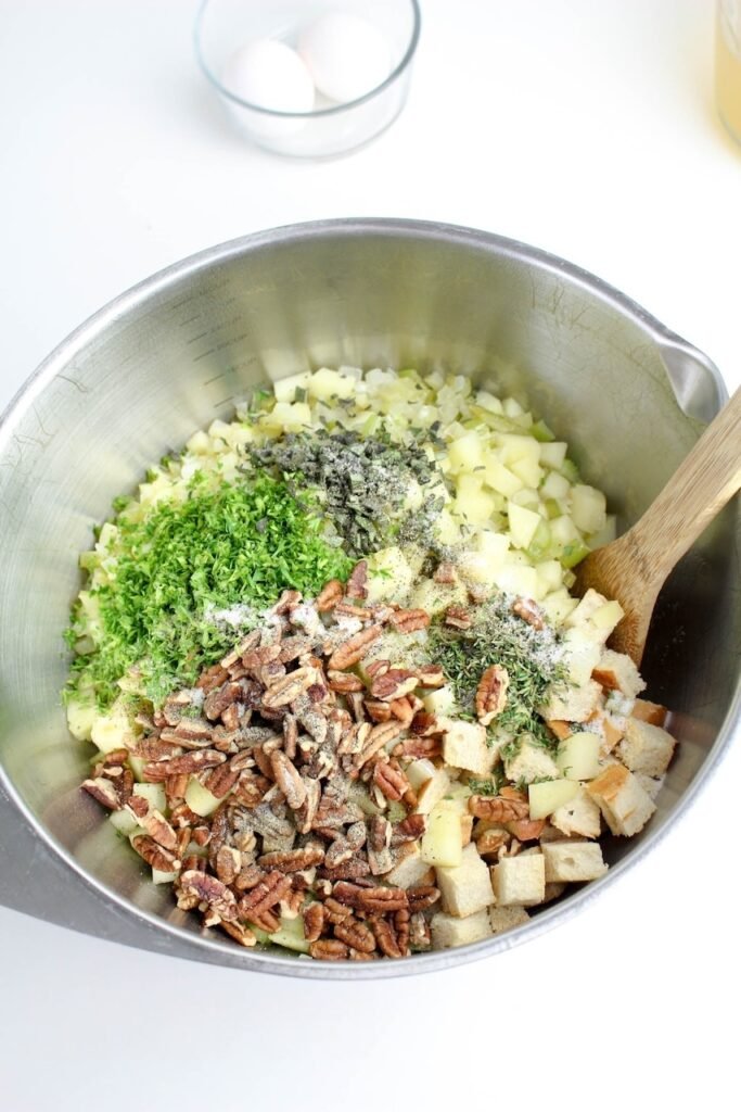Mixing bread cubes, sautéed apples, celery, onions, fresh herbs, and pecans in a large bowl.