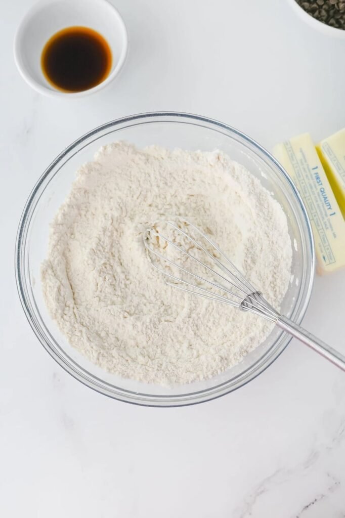 Mixing flour and salt in a glass bowl with a whisk while preparing holiday dessert.