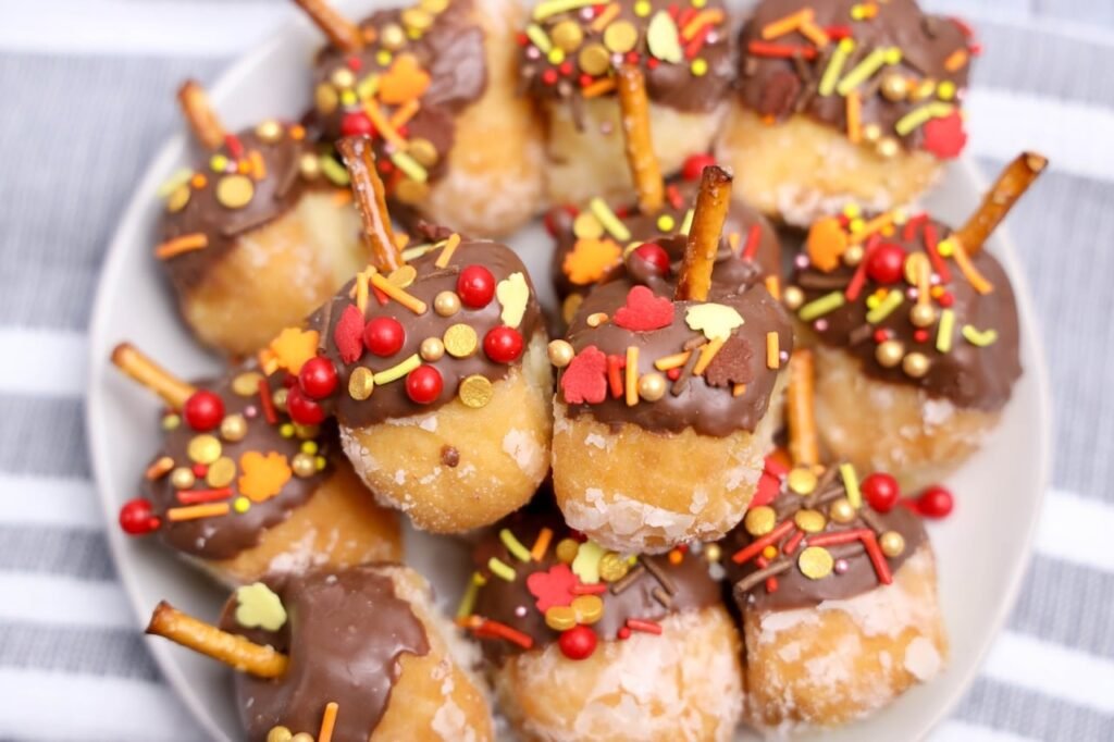 Plate of no-bake acorn donut holes decorated with chocolate, pretzel stems, and colorful fall sprinkles.
