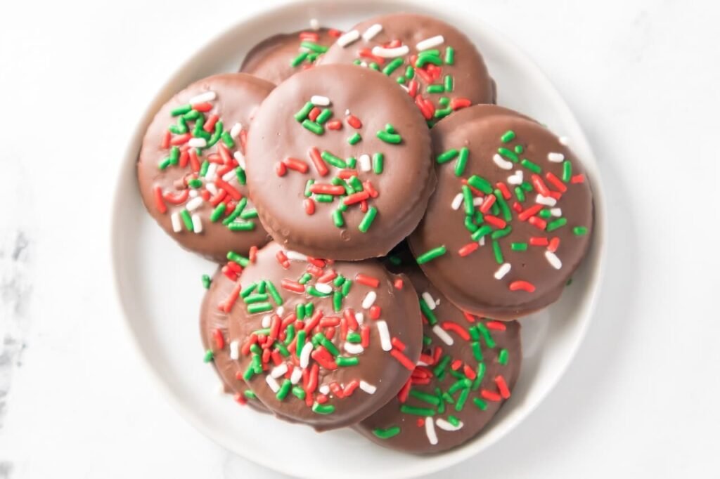 Overhead photo of a plate filled with chocolate-covered Christmas Thin Mint Cookies topped with red, green, and white sprinkles, showing an easy no-bake holiday cookie made with Ritz crackers and mint chocolate.