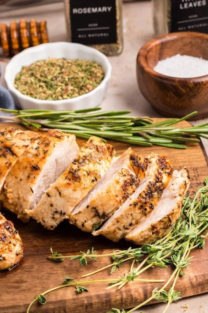 Sliced oven roasted turkey tenderloin on a wooden cutting board with rosemary, thyme, and seasonings in the background.