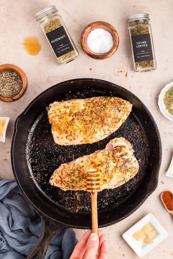 Seared breast in a cast-iron skillet being drizzled with honey for a golden glaze before oven roasting.