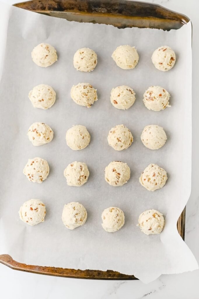 Rolled pecan snowball cookie dough balls arranged evenly on a parchment-lined baking sheet before chilling and baking.