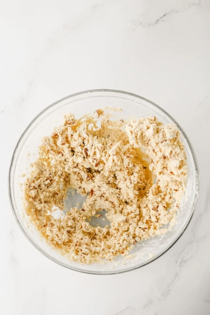 Mixed dough in a glass bowl showing creamy texture with finely chopped toasted pecans evenly distributed.