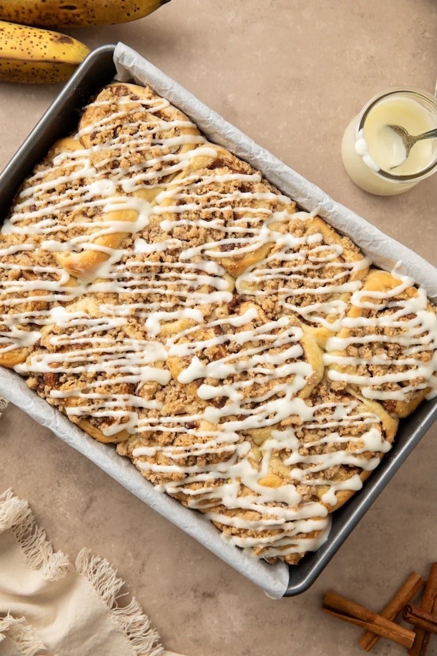 Freshly baked pumpkin cinnamon rolls in a pan topped with streusel and cream cheese icing drizzle