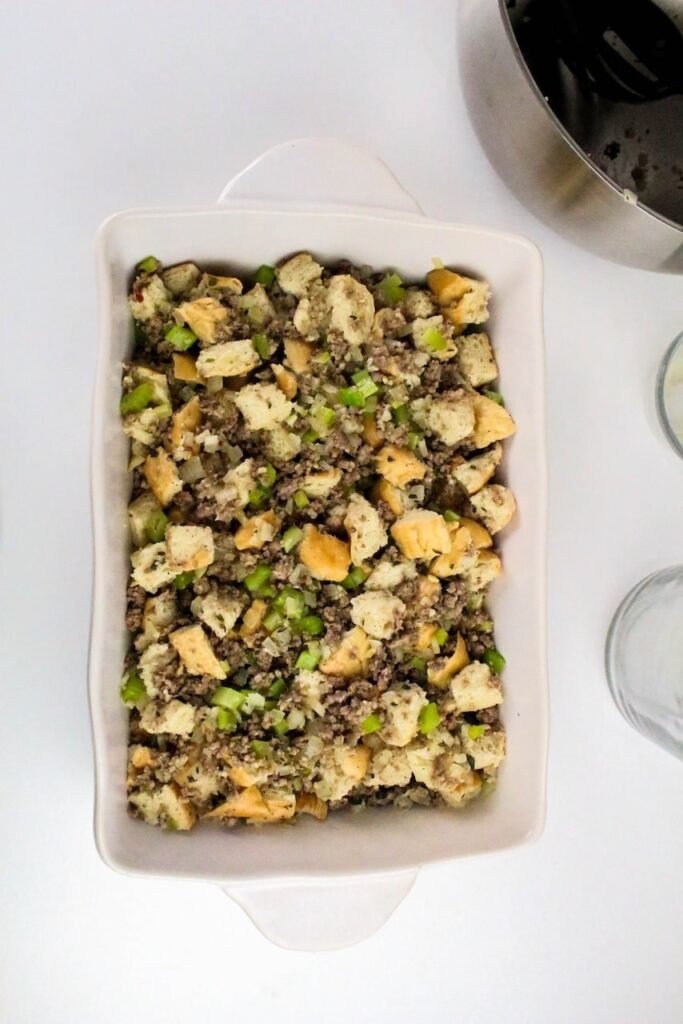 Unbaked mixture with bread cubes, celery, and sausage in a white casserole dish ready for the oven.