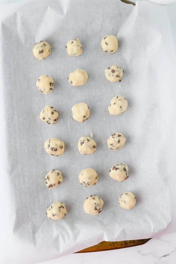 Unbaked chocolate chip snowball cookie dough balls arranged on a parchment-lined baking sheet before baking.