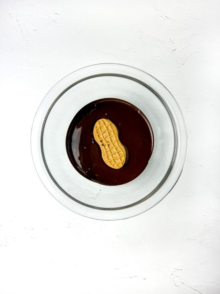 Nutter Butter cookie being dipped into a bowl of melted chocolate to coat it for owl cookie recipe.