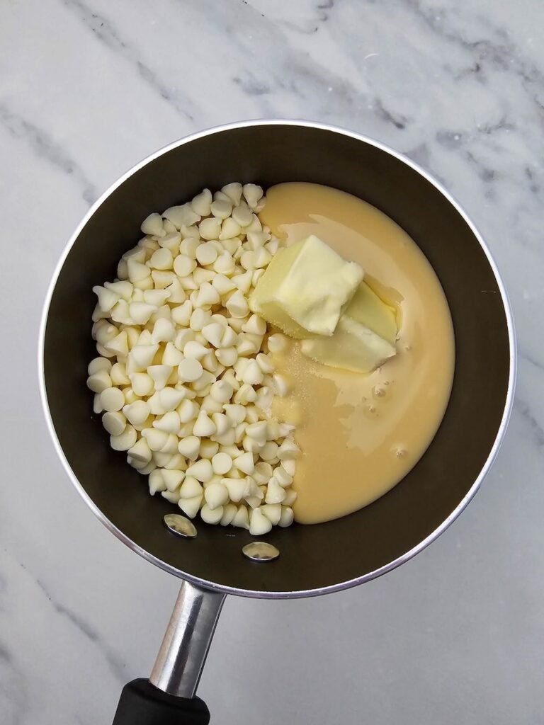 White chocolate chips, butter, and sweetened condensed milk in a saucepan ready to melt.